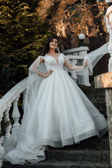 Fototapeta premium Beautiful lady in luxurious ballroom dress walking up the stairs. Charming autumn bride. Beautiful woman with professional make up and hair style. Attractive young woman enjoying her time. 