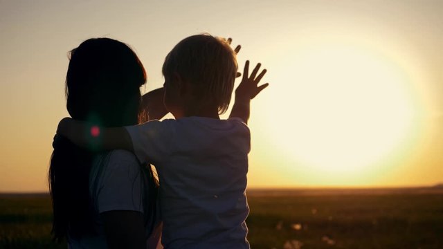 Happy family in a field at sunset. Mom with a son stretch their hands to the sun while playing with the rays. The concept of a happy family and togetherness with nature. Team Family Work