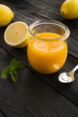 Lemon kurd in the glass jar on the black wooden background. Location vertical.