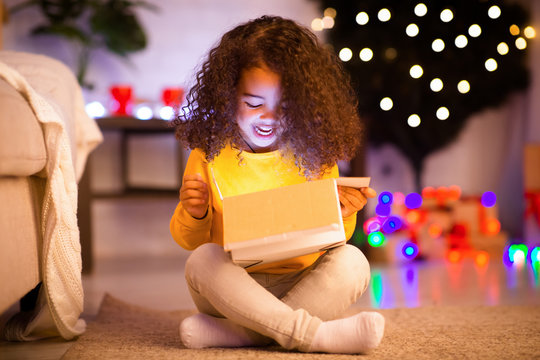 Surprised little african girl opening glowing Christmas gift