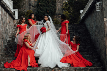 Group portrait of bride and bridesmaids on the stairs. Wedding in autumn. Bride in wedding dress and bridesmaids in red dresses at wedding day. Stylish wedding in red color. Marriage concept.
