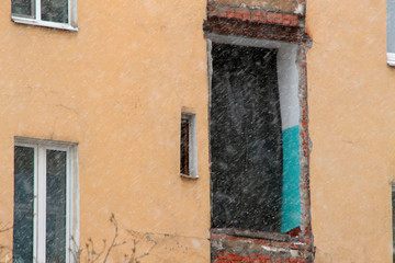 Fototapeta na wymiar Wall of a yellow house with a broken doorway during snowfall