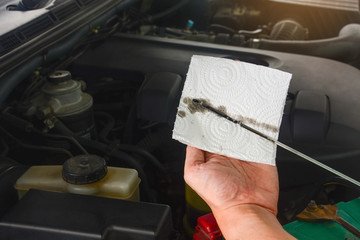 close up auto mechanic's hand checks the level and color of engine oil in a car engine during maintenance