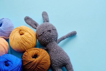 Bright color yarn clews with grey stuffed amigurumi bunny on the blue background. Concept of amigurumi toy making, handcrafting, knitting, hobbie