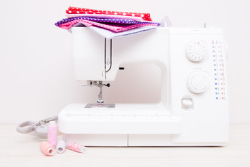 white professional sewing machine on the table, fabrics for girls, scissors and spools of thread, front view, copy space,white background