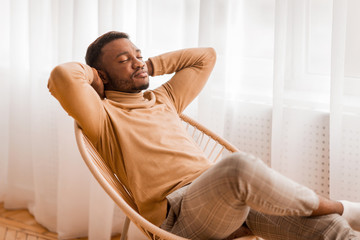 Man Sitting On Chair Holding Hands Behind Head At Home