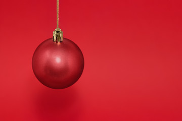 Red Christmas bauble hanging from gold string isolated against a red background, with copy space