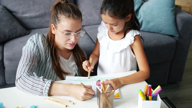 Happy family daughter and mother drawing picture at table in apartment, joyful kid is smiling enjoying hobby and mother's help. People and lifestyle concept.