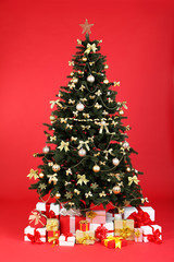 Christmas fir tree with ornaments and gift boxes on red background