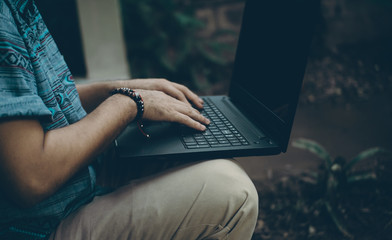 Young Hispanic man on the sidewalk of his house checking the black computer