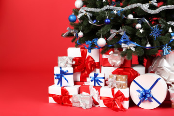 Christmas fir tree with ornaments and gift boxes on red background