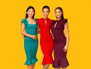 Fototapeta premium Three Diverse Girls In Glamourous Dresses Posing Over Yellow Background