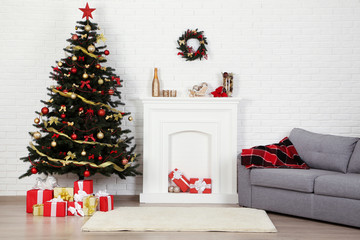 Christmas fir tree with ornaments and gift boxes near decorated fireplace at home