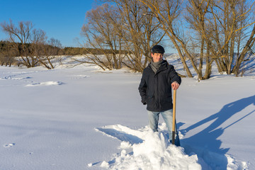 Handsome middle-aged caucasian man cleaning snow on household plot in sunny day. Man with shovel...