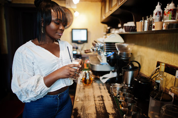 Stylish african american women in white blouse and blue jeans posed at cafe with caramel latte.