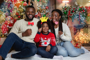 Black family of three posing with photo props near Xmas tree