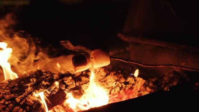 CU of girl roasting marshmallows on a cosy campfire using stick. The Marshmallows catch fire and she blows them out. Filmed on RED camera, Slow motion.