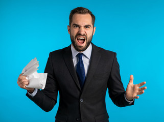 Serious businessman tearing contract in pieces. Angry furious male office worker throwing crumpled paper, having nervous breakdown at work, screaming in anger, stress management. 