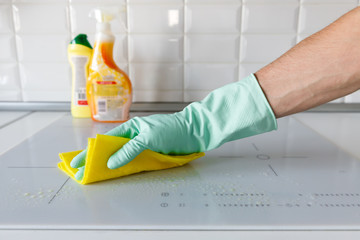 Close up of man hand in protective rubber gloves washing or cleaning modern white induction hob by...