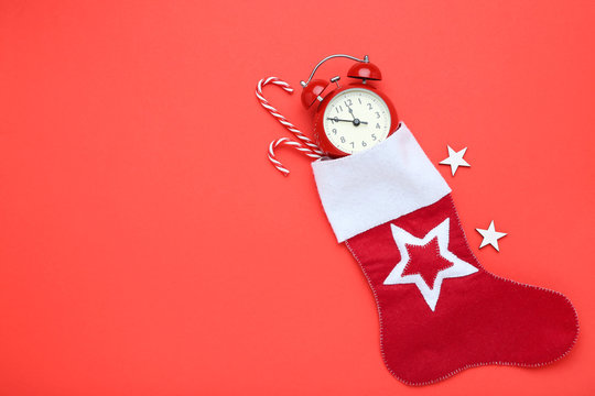 Red christmas stocking with candy canes and alarm clock on red background