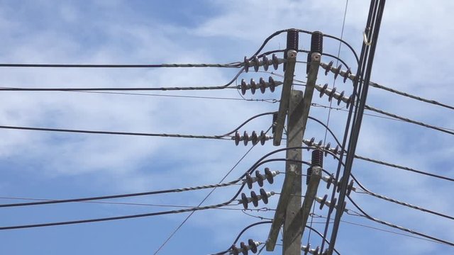 CLOSE UP: Concrete electricity pole towers into the bright blue summer sky. Tall telegraph post providing electricity to nearby towns in Thailand. Dangerous power cables running above a sunny street.