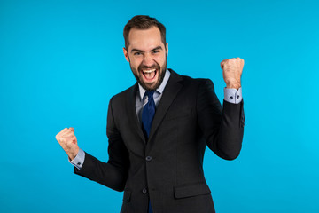 Yes winner gesture. Amazed european businessman with beard shocked, saying yeah. Handsome guy with stylish hairdo and beard surprised to camera over blue background.