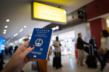 Close up of woman holding an Hong Kong passport over a blurred airport background. Digital composite