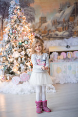 Obraz na płótnie Canvas pretty happy blonde girl with curls of 6-7 years in a thematic holiday Christmas sweater with snowmen, holding snow in her hands, Christmas, near the New Year tree, winter