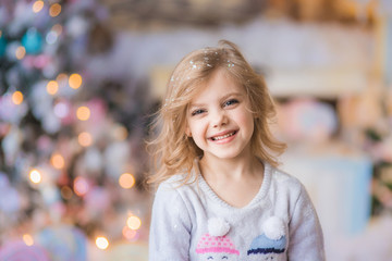 Portrait of a fair-haired beautiful curly happy smiling girl 6-7 years old in a New Year's Eve on Christmas Eve against a background of lights