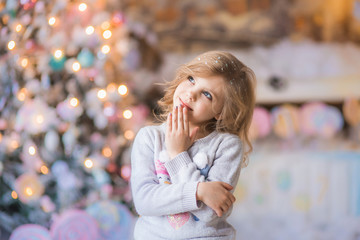 Portrait of a fair-haired beautiful curly happy smiling girl 6-7 years old in the New Year's Eve on Christmas Eve against the background of lights, looking up thoughtfully, dreaming