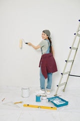 Happy young Vietnamese woman painting room walls with roller and smiling at camera