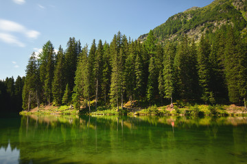 Emerald green waters of an alpine lake in the forest. Crystal clear water of beautiful Lake Schwarzwassersee near Ischgl, Paznaun region, Tyrol, Austria.
