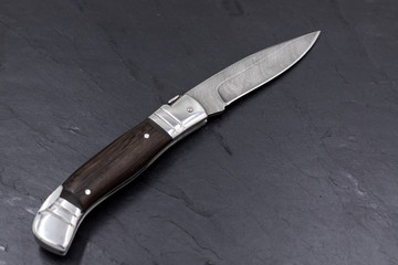 Damascus steel knife on black slate board. Damascus steel hunting knife with wooden handle.