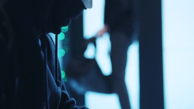 Computer spy typing green code on notebook trying to hack server system of data center. Close-up masked hacker copying secret data from server cabinet inside database .