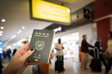 Close up of woman holding a South Korea passport over a blurred airport background. Digital composite. South Korea has the third world most powerful passport, according to the Henley passport index - obrazy, fototapety, plakaty