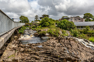 Female cyclist admiring the Clifden waterfalls on the Owenglen river with the old Ardbear bridge surrounded by green trees in the background, spring day in the province of Connacht, Ireland