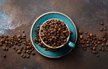 Natural organic roasted coffee beans in blue cup on dark rusty background.