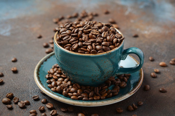 Natural organic roasted coffee beans in blue cup on dark rusty background.