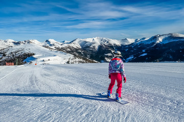 Snowboarding girl going down the slope in Bad Kleinkirchheim, Austria. The slopes are perfectly groomed.There is a ski lift above the girl. Lots of snow caped mountains. Winter sports activity in Alps