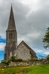 Fototapeta na wymiar Christ church on a hill with its bell tower and surrounded by a stone fence, cloudy spring day in Clifden, province of Connacht, Ireland