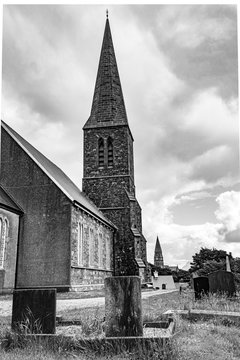 Rear view of the church of Christ with its cemetery and crypts with the bell tower of the church of St. Joseph in the background, cloudy spring day in Clifden, Ireland, black and white image