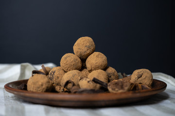 Handmade chocolate truffles on vintage clay plate with fragrant spices on dark background