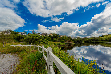 Wooden fence next to a path in the Clifden bay with clouds reflecting in the water and the village...