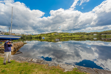 Clifden harbor with anchored boats and clouds reflecting in the water at high tide, a photographer...
