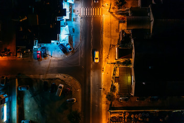 Aerial top view of night illuminated road with car in mediterranean town in evening, drone photo.