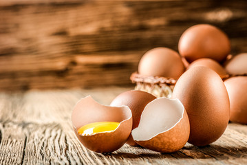 Fresh brown eggs on wooden table. Broken egg with yolk