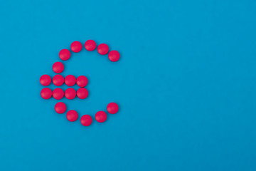 Euro sign made from pink pills. Copyspace on a blue background. Pharmaceutical trade concept.