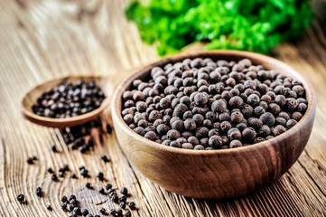 Black pepper. Black dry pepper in wooden bowl on wood table with green background.
