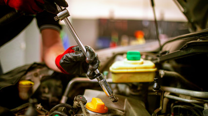 Automobile repair shop employee changing a spark plug in a car at the garage.