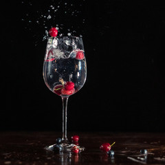 Gin and cherry cocktail in a glass with red fruits splashing taken in studio with a dark background at a party